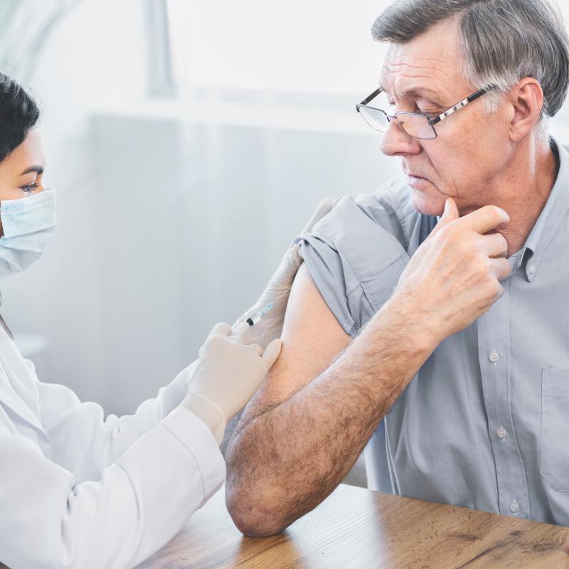 Nurse giving imunisation injection to older male patient